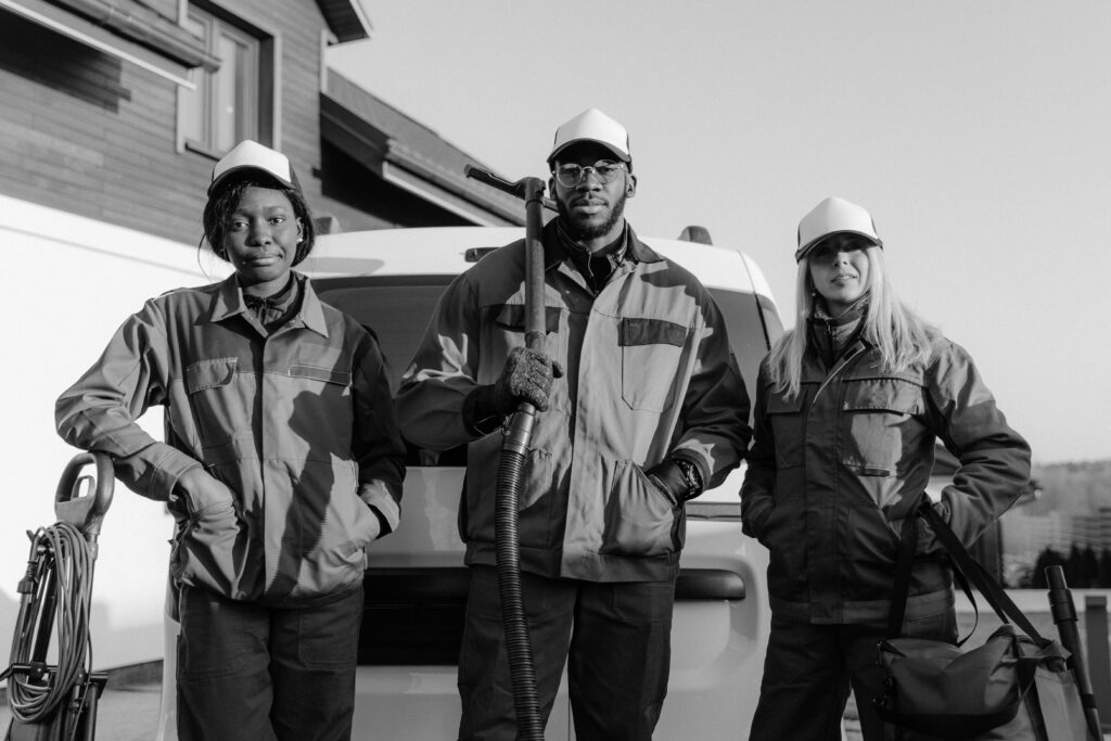pexels-photo-6196225-6196225-1 Three professional cleaners in uniform pose with equipment in front of a building.
